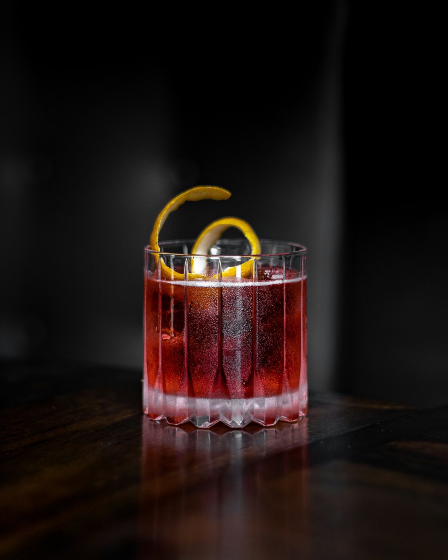 A stirred red cocktail with a lemon twist